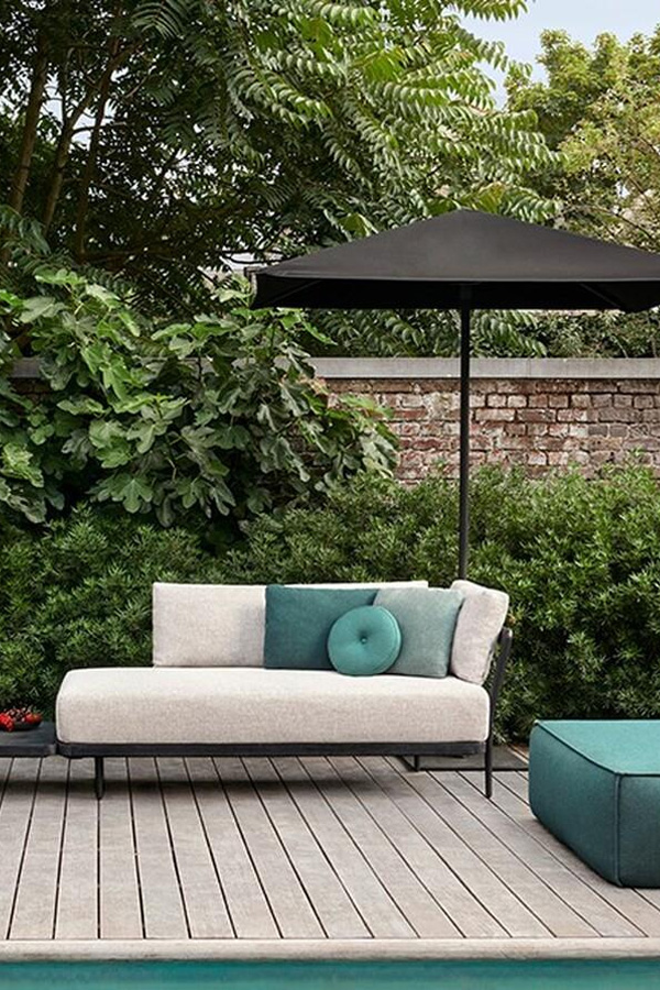 Salon de jardin gris avec un pouf bleu sur une terrasse en parquet avec un parasol noir
