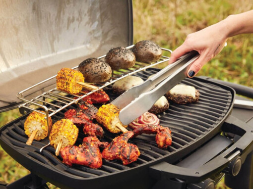 Une dame retourne les maïs qui cuisent sur le barbecue au gaz